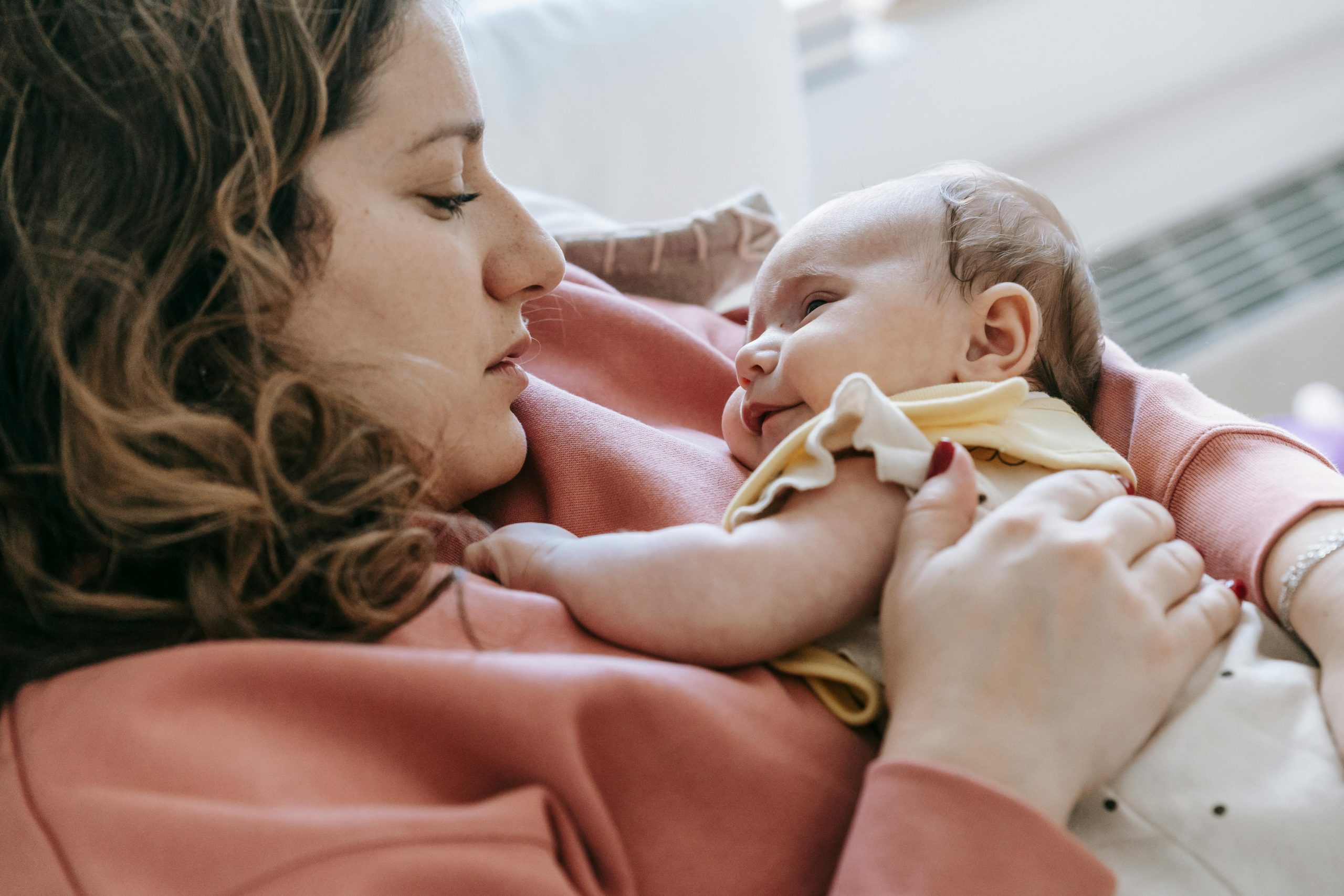Tender moment of a mother embracing her baby indoors, showcasing love and care.